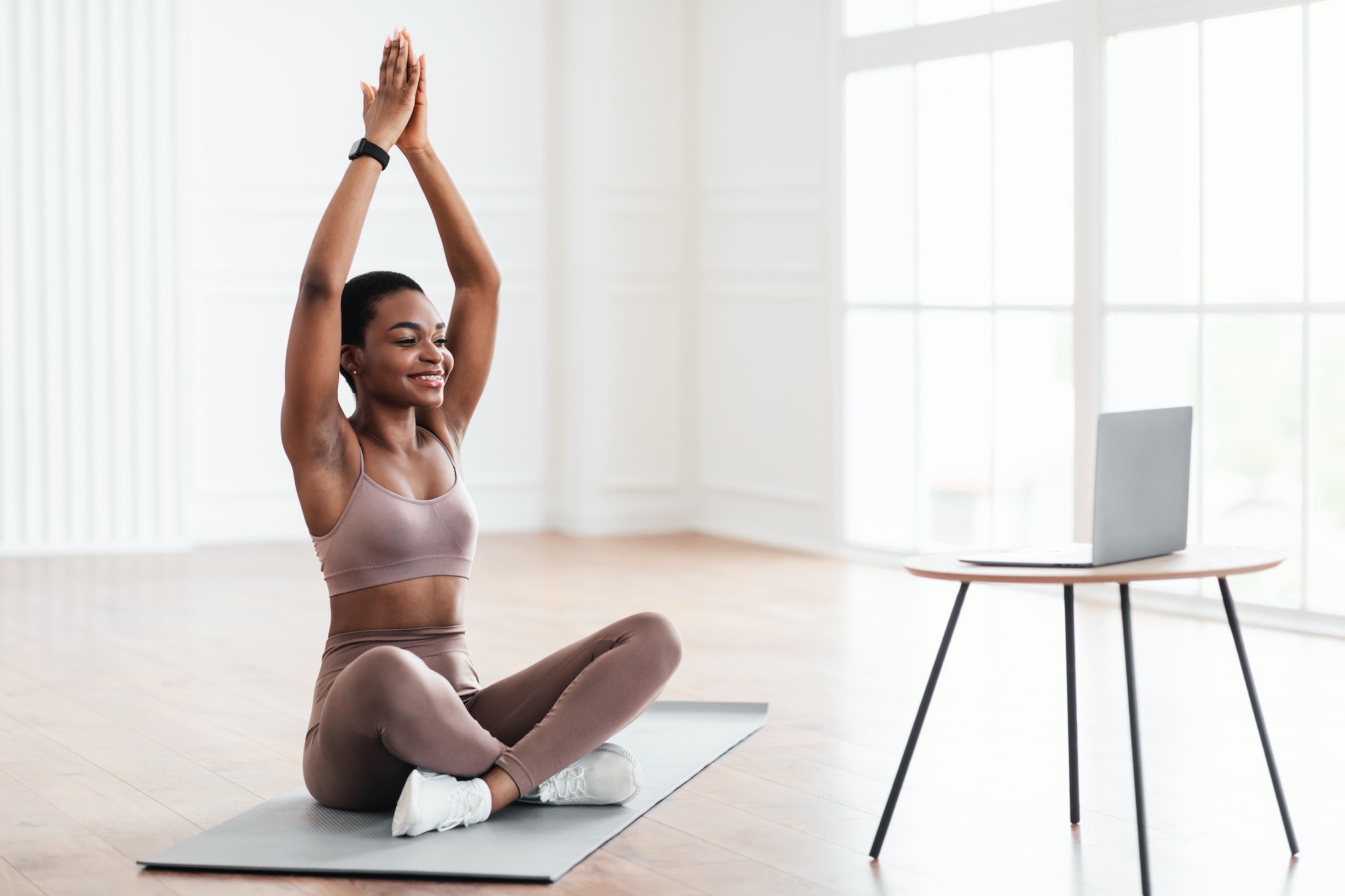 Smiling young black woman sitting on yoga mat using laptop